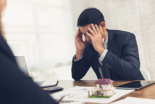 A man in a suit with his head in his hands because a seller breached a real estate contract
